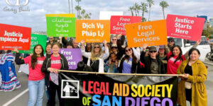10 Things About Joanne L. Franciscus & Legal Aid Society of San Diego LASSD staff members in a parade holding up signs in several languages reading "Justice Starts Here"